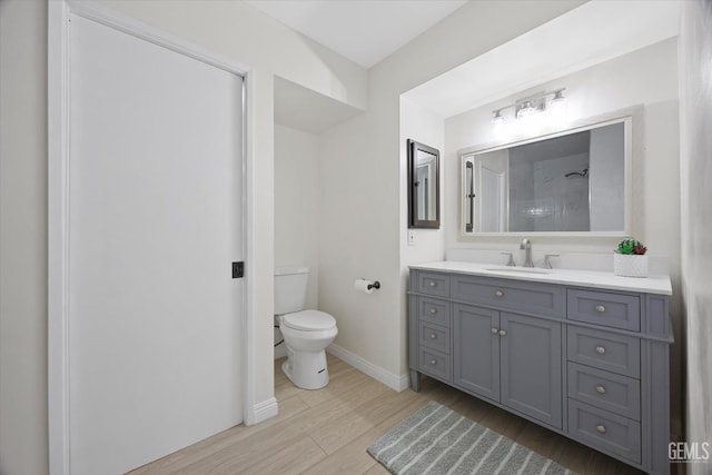 bathroom with toilet, wood finished floors, vanity, baseboards, and a shower