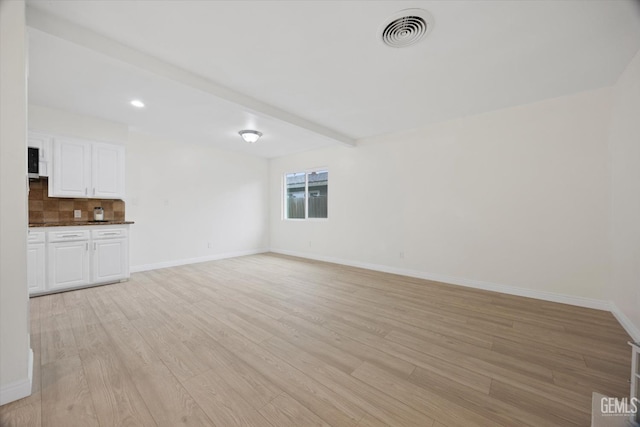 unfurnished living room featuring light wood-type flooring, baseboards, visible vents, and beam ceiling