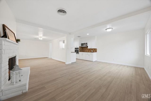 unfurnished living room with light wood-type flooring, baseboards, a fireplace, and visible vents