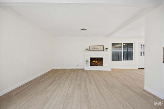 unfurnished living room with light wood-style flooring, a brick fireplace, visible vents, and baseboards