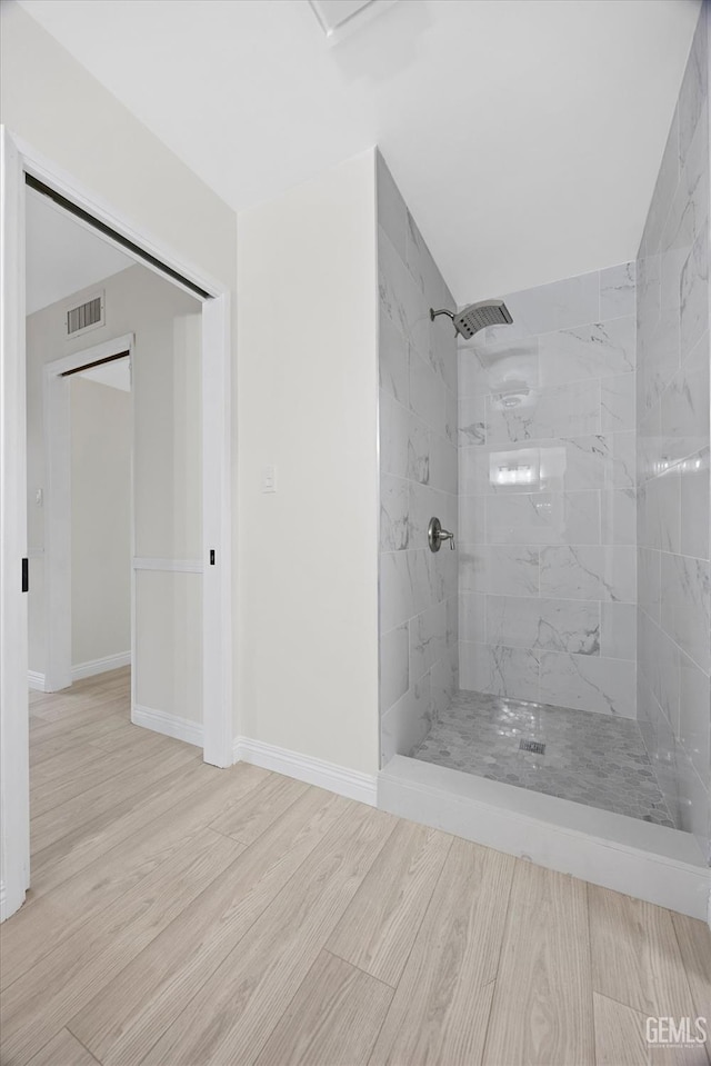 full bath with tiled shower, wood finished floors, visible vents, and baseboards