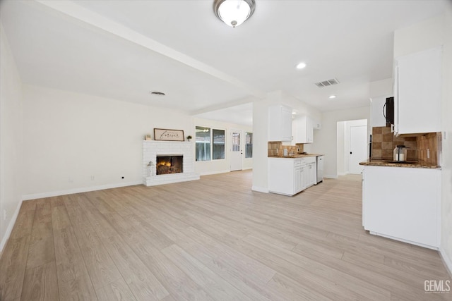 unfurnished living room with light wood-type flooring, a brick fireplace, visible vents, and baseboards