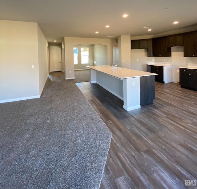 kitchen with dark hardwood / wood-style floors, dark brown cabinets, sink, and a center island with sink