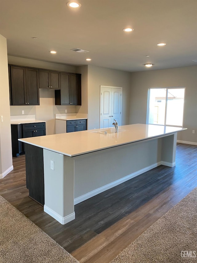 kitchen featuring sink, dark brown cabinetry, dark hardwood / wood-style floors, and a center island with sink