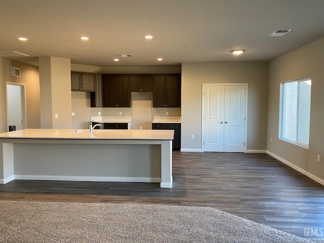 kitchen with sink, dark brown cabinets, dark hardwood / wood-style floors, and a kitchen island with sink