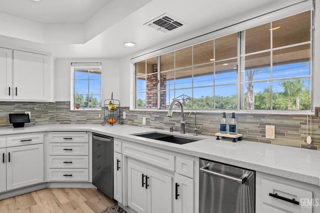 kitchen with white cabinets, dishwasher, light stone countertops, and sink