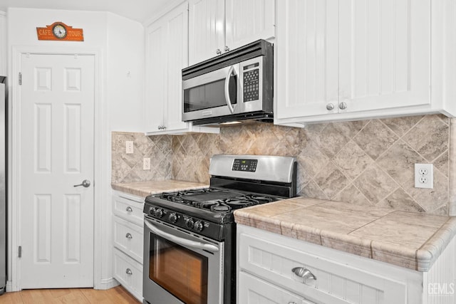 kitchen featuring appliances with stainless steel finishes, backsplash, white cabinets, light hardwood / wood-style floors, and tile counters