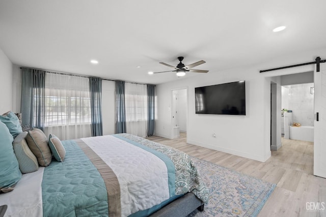 bedroom featuring ceiling fan, light hardwood / wood-style floors, ensuite bathroom, and a barn door