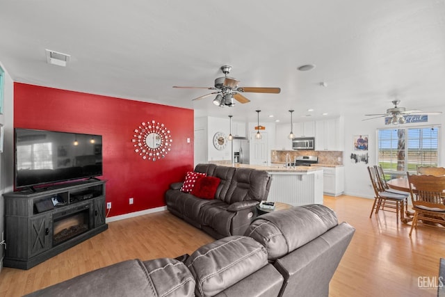 living room featuring sink, light wood-type flooring, and ceiling fan