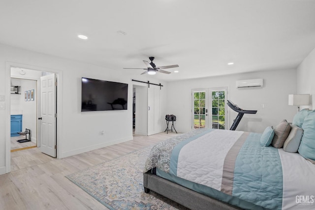 bedroom with ceiling fan, french doors, light wood-type flooring, a barn door, and a wall mounted air conditioner