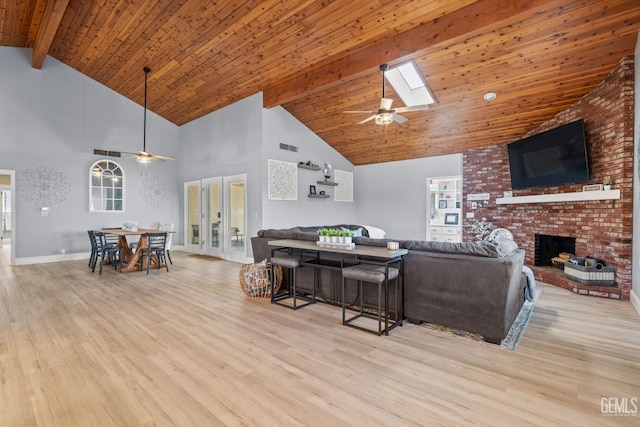 living room featuring beam ceiling, a brick fireplace, high vaulted ceiling, a skylight, and light hardwood / wood-style floors