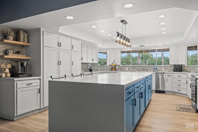 kitchen featuring white cabinets, decorative light fixtures, blue cabinetry, and a tray ceiling