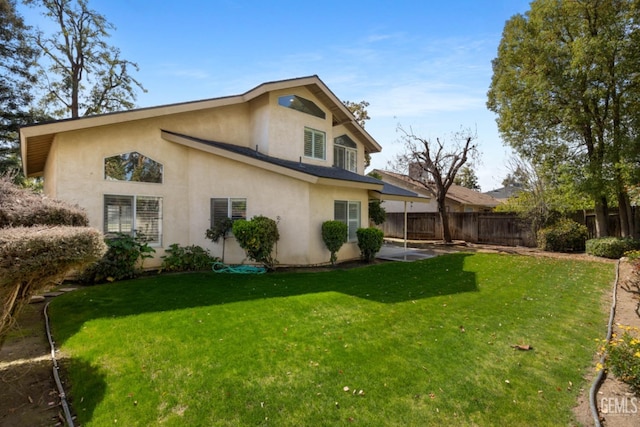 back of property featuring stucco siding, a lawn, a patio, and fence