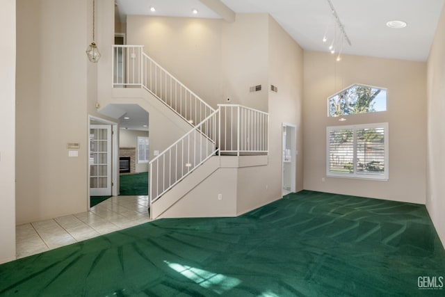 carpeted entryway with stairway, a high ceiling, visible vents, and a glass covered fireplace