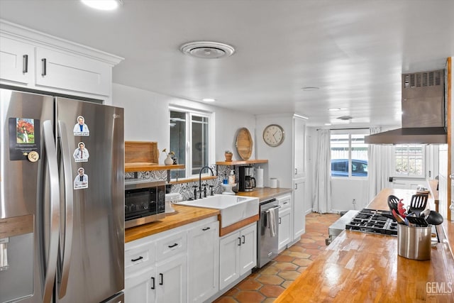 kitchen with butcher block counters, white cabinetry, sink, stainless steel appliances, and extractor fan