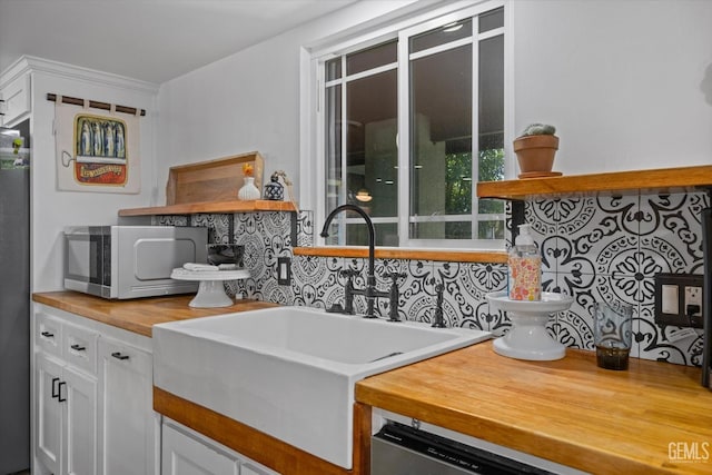 kitchen featuring decorative backsplash, wooden counters, stainless steel dishwasher, sink, and white cabinets