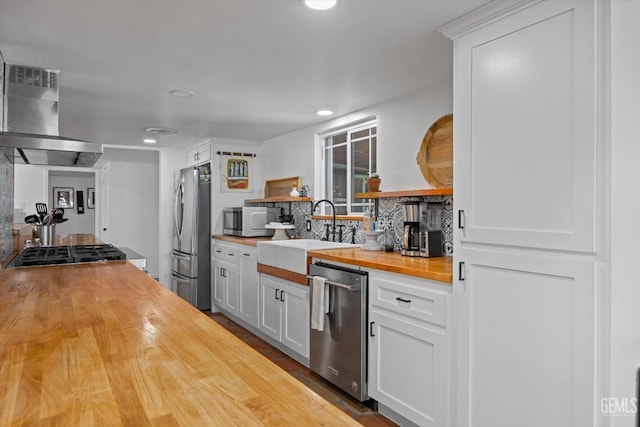 kitchen featuring butcher block counters, sink, extractor fan, white cabinets, and appliances with stainless steel finishes