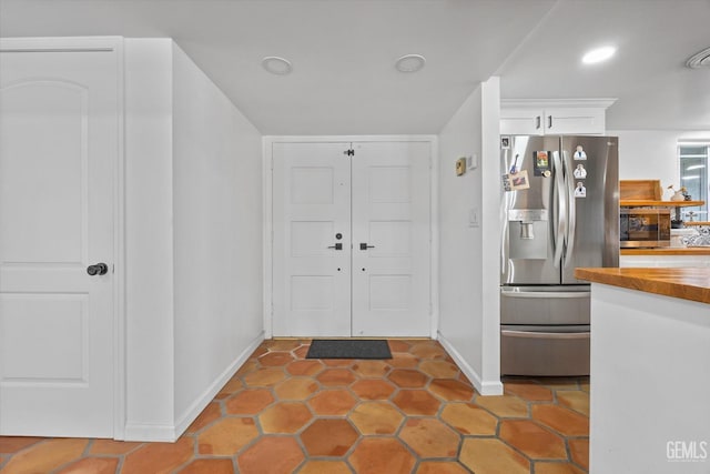 kitchen featuring white cabinets, stainless steel fridge, light tile patterned flooring, and butcher block counters