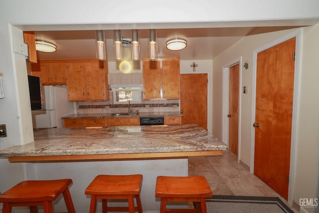 kitchen with brown cabinetry, a peninsula, tasteful backsplash, a sink, and dishwasher