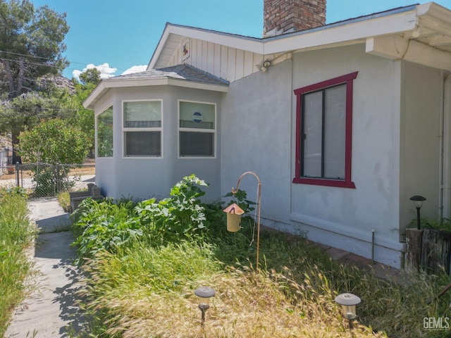 view of side of property with fence, a chimney, and stucco siding
