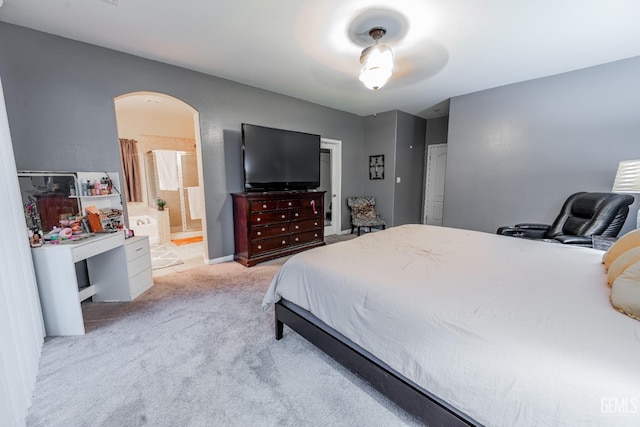 bedroom featuring ensuite bath, arched walkways, baseboards, and light colored carpet