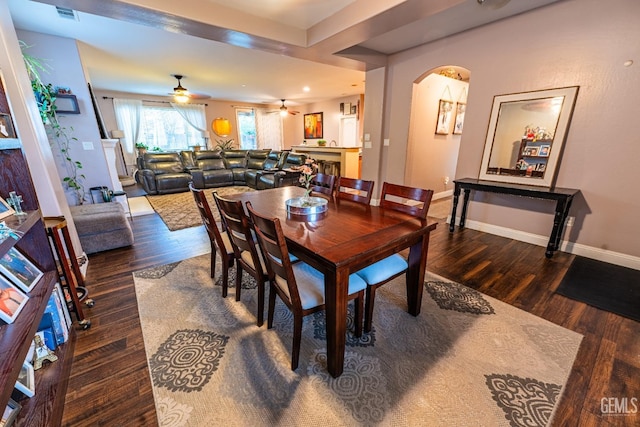 dining space featuring arched walkways, a ceiling fan, visible vents, baseboards, and dark wood finished floors