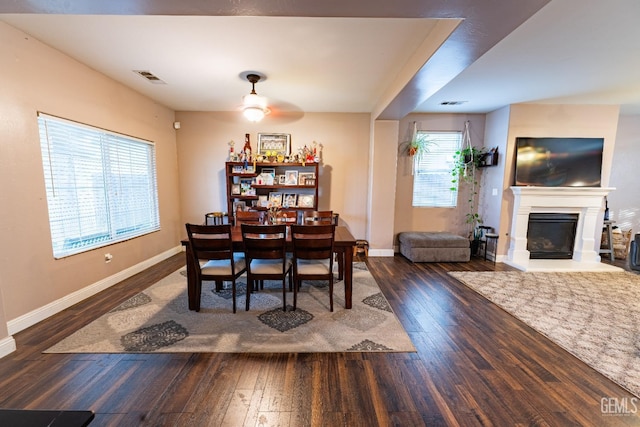 dining area with dark wood-type flooring, a glass covered fireplace, visible vents, and baseboards