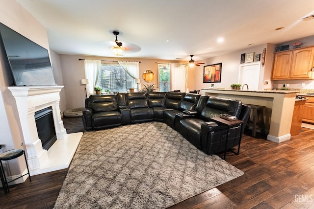 living room with dark wood-style flooring, a glass covered fireplace, and a ceiling fan