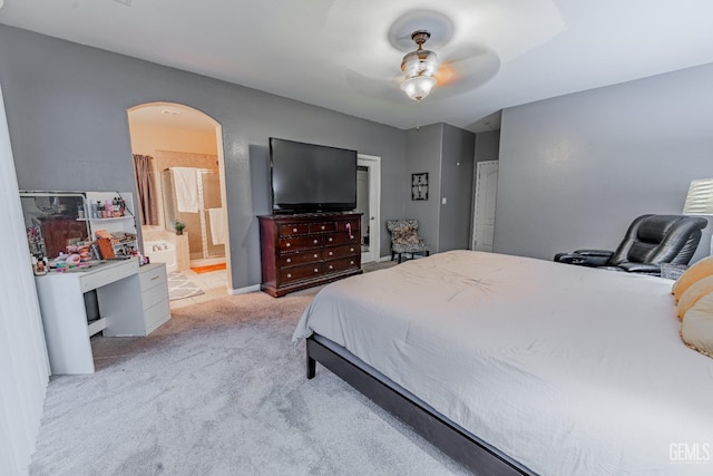 bedroom featuring arched walkways, light colored carpet, ceiling fan, and ensuite bath