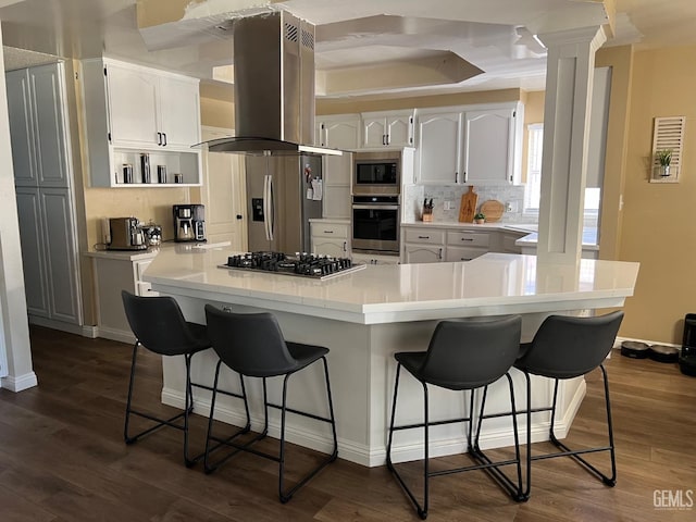 kitchen featuring a breakfast bar, island exhaust hood, stainless steel appliances, backsplash, and white cabinetry