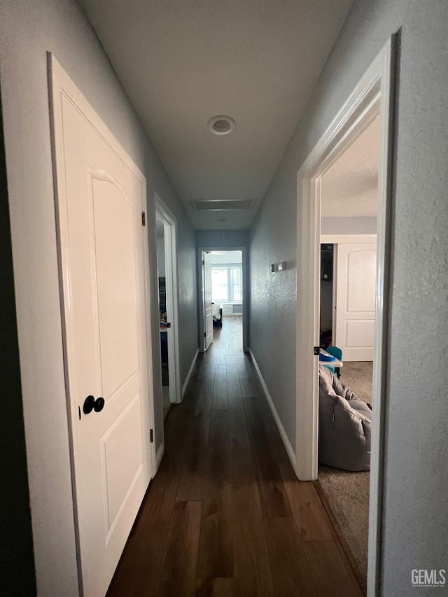 corridor featuring baseboards and dark wood-type flooring