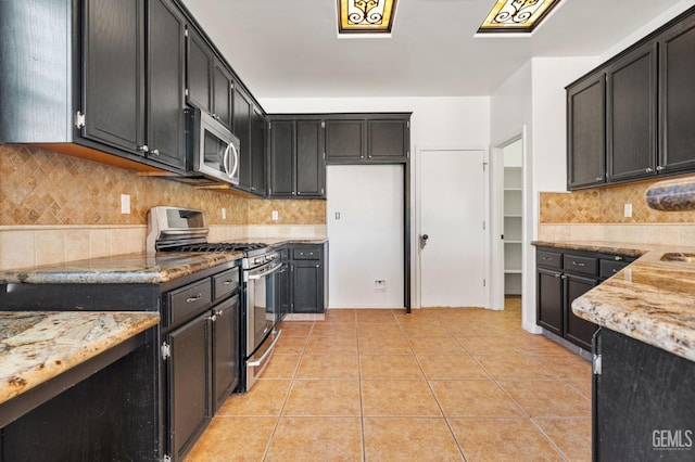 5219 Port Dr, Bakersfield, CA 93312 - kitchen with appliances with stainless steel finishes, light stone countertops, light tile patterned floors, dark cabinetry, and decorative backsplash