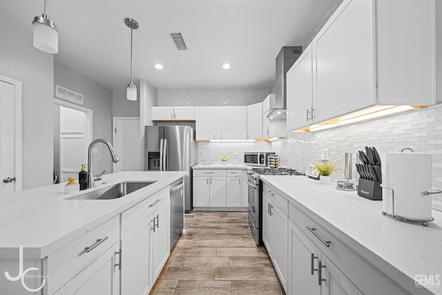 kitchen with stainless steel appliances, light countertops, wall chimney range hood, a sink, and visible vents