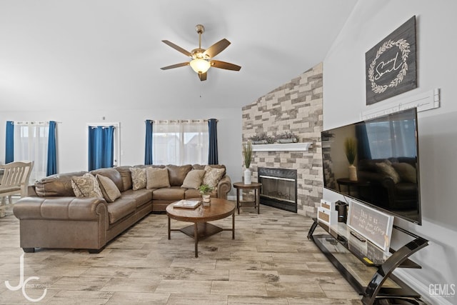 living room with plenty of natural light, a ceiling fan, a stone fireplace, and vaulted ceiling