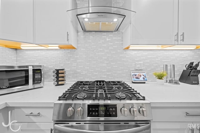 kitchen featuring decorative backsplash, light stone counters, wall chimney range hood, white cabinets, and appliances with stainless steel finishes