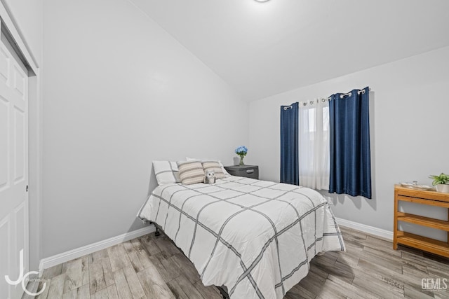 bedroom with vaulted ceiling, wood finished floors, and baseboards