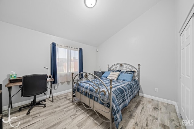 bedroom featuring a closet, light wood-style flooring, vaulted ceiling, and baseboards
