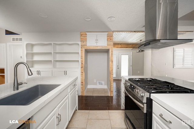 kitchen with gas stove, island range hood, sink, light tile patterned floors, and white cabinetry