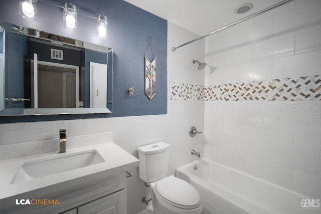 full bathroom featuring tiled shower / bath combo, toilet, tile walls, and vanity