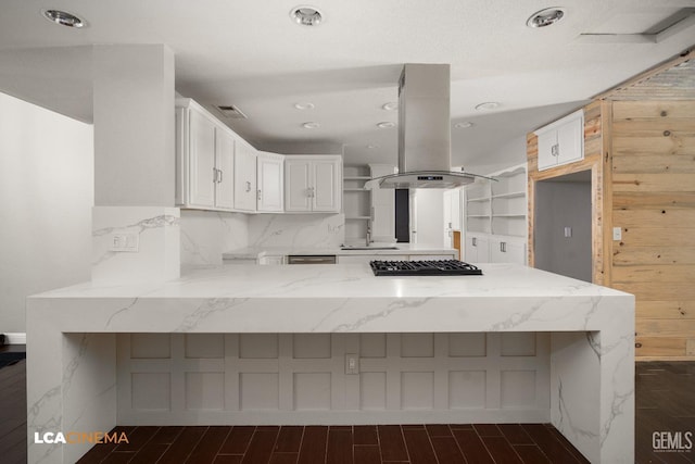 kitchen featuring light stone counters, island exhaust hood, kitchen peninsula, stainless steel gas stovetop, and white cabinets