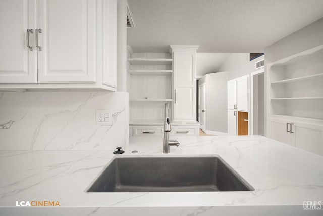 kitchen featuring white cabinetry, light stone countertops, sink, and a textured ceiling