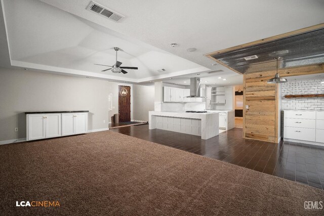 interior space with wall chimney exhaust hood, a tray ceiling, ceiling fan, dark colored carpet, and white cabinetry