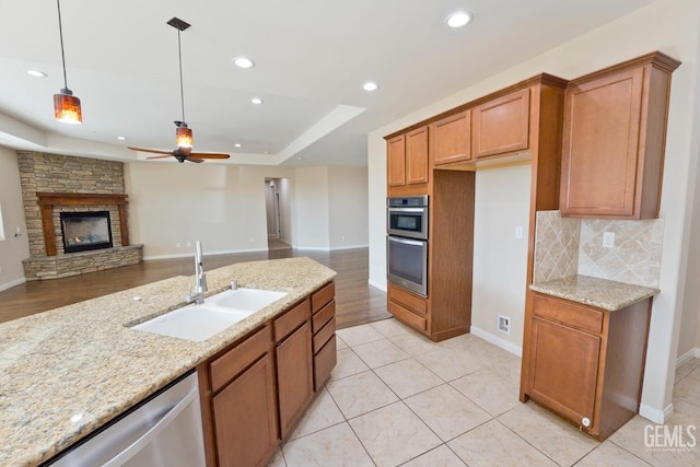 kitchen featuring appliances with stainless steel finishes, a stone fireplace, light stone countertops, and sink