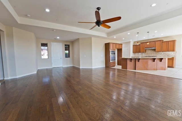 unfurnished living room featuring sink, light hardwood / wood-style flooring, a raised ceiling, and ceiling fan