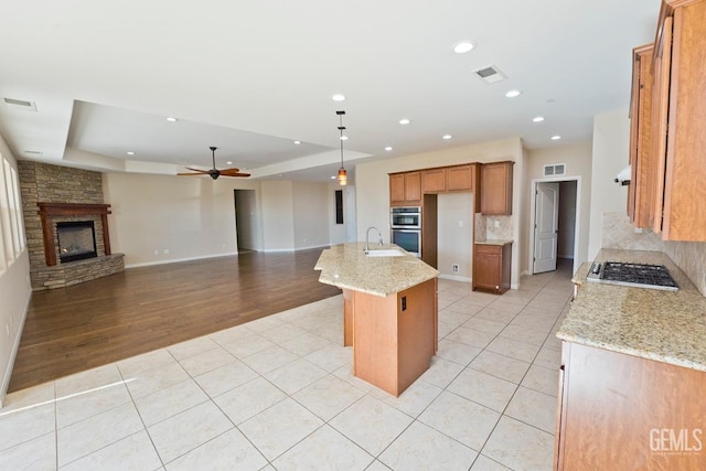 kitchen with an island with sink, light stone countertops, sink, and light tile patterned floors