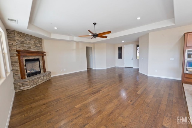 unfurnished living room with dark hardwood / wood-style floors, ceiling fan, a fireplace, and a raised ceiling