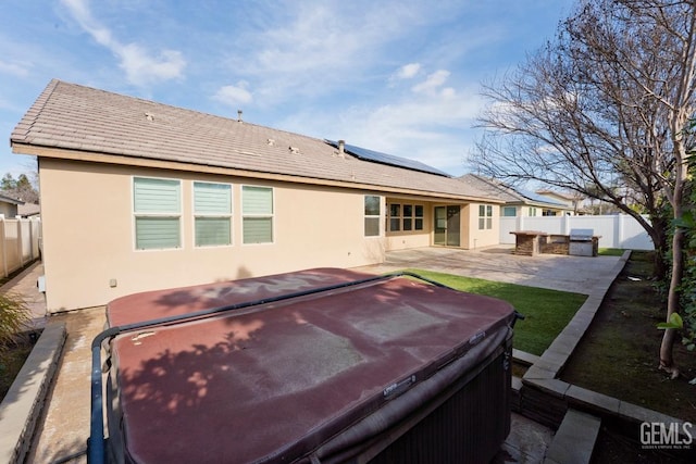 back of house with a hot tub, a patio, and solar panels