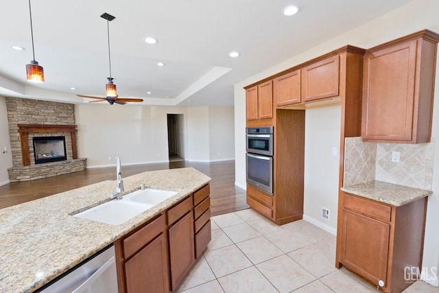 kitchen featuring sink, appliances with stainless steel finishes, a fireplace, light stone countertops, and decorative light fixtures