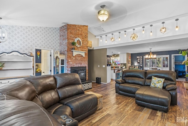 living room with lofted ceiling, wood-type flooring, a notable chandelier, and a brick fireplace