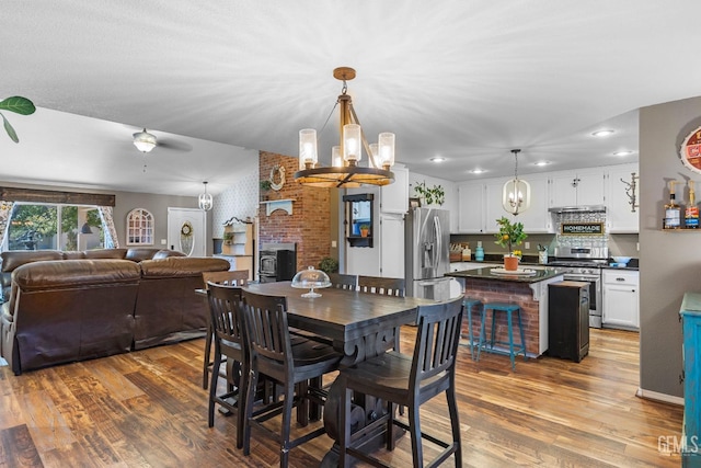 dining room featuring brick wall, a wood stove, wood-type flooring, and a chandelier